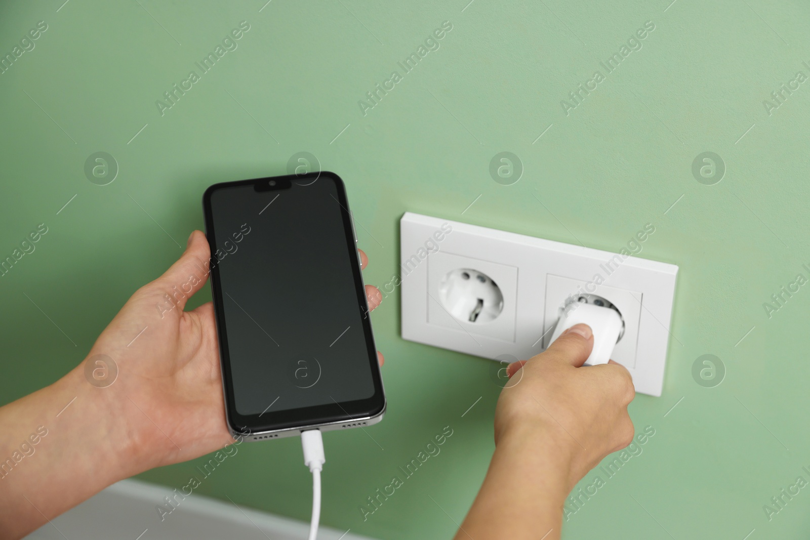 Photo of Woman plugging smartphone into power socket indoors, closeup