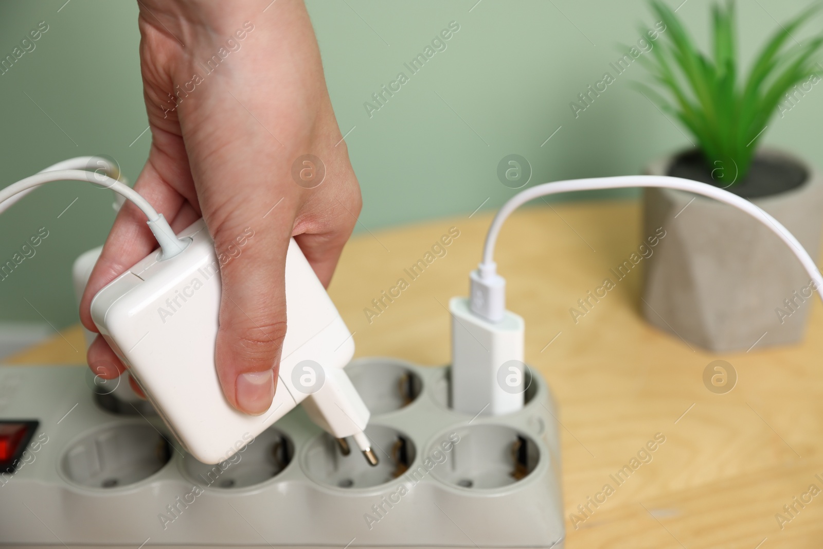 Photo of Woman plugging USB adapter with cable into power strip at table, closeup