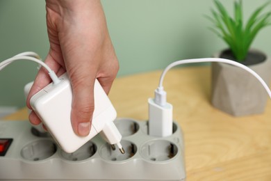 Photo of Woman plugging USB adapter with cable into power strip at table, closeup