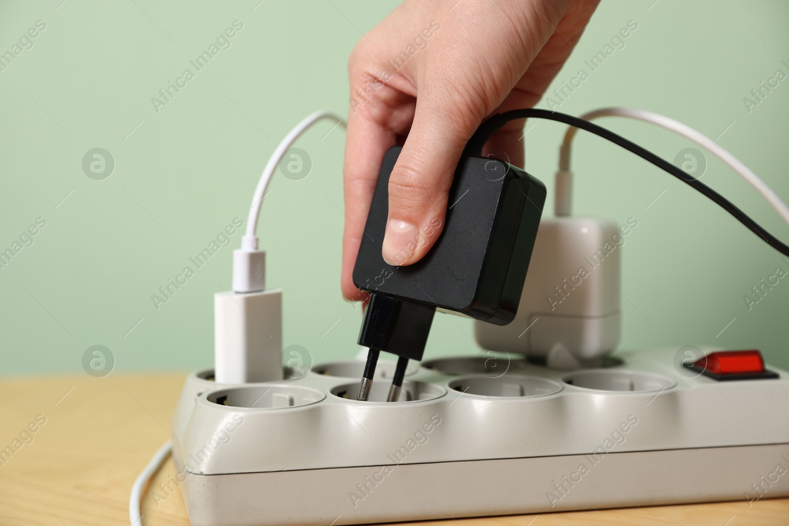 Photo of Woman plugging USB adapter with cable into power strip at table, closeup