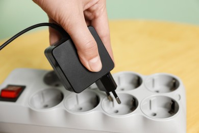 Photo of Woman plugging USB adapter with cable into power strip at table, closeup
