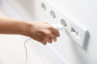 Photo of Woman plugging USB adapter with cable into power socket on white wall, closeup
