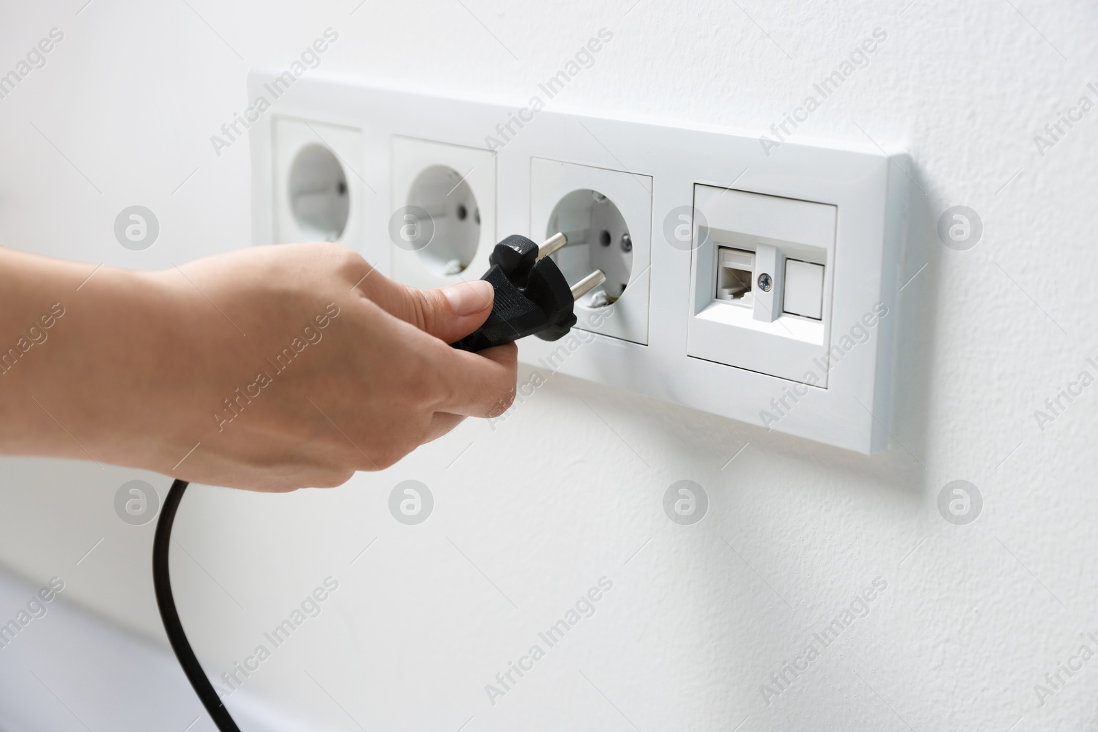 Photo of Woman putting plug into power socket on white wall, closeup