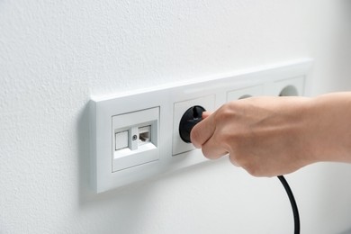 Photo of Woman putting plug into power socket on white wall, closeup
