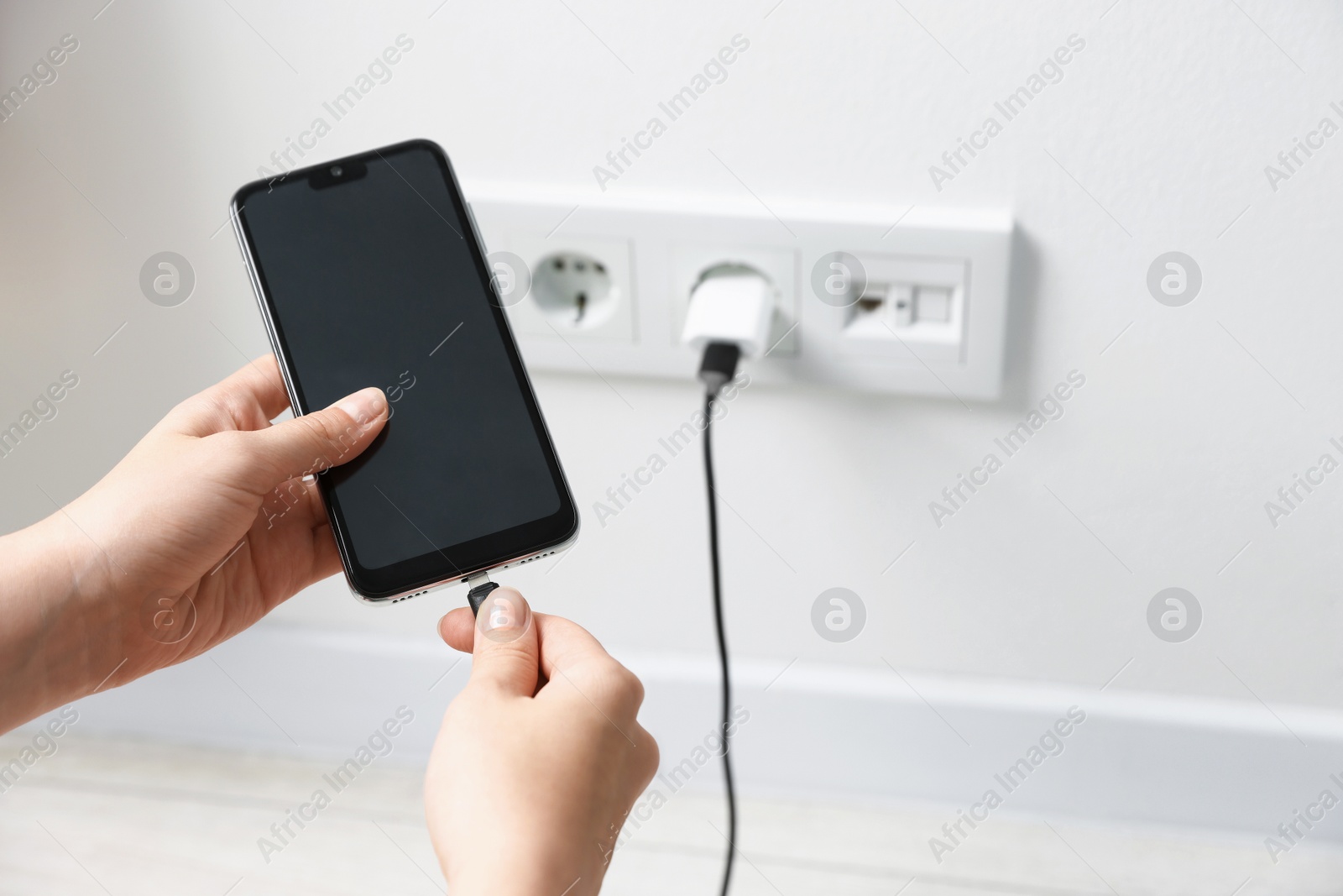 Photo of Woman connecting charging cable to smartphone indoors, closeup