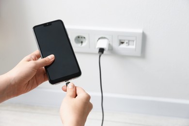 Photo of Woman connecting charging cable to smartphone indoors, closeup