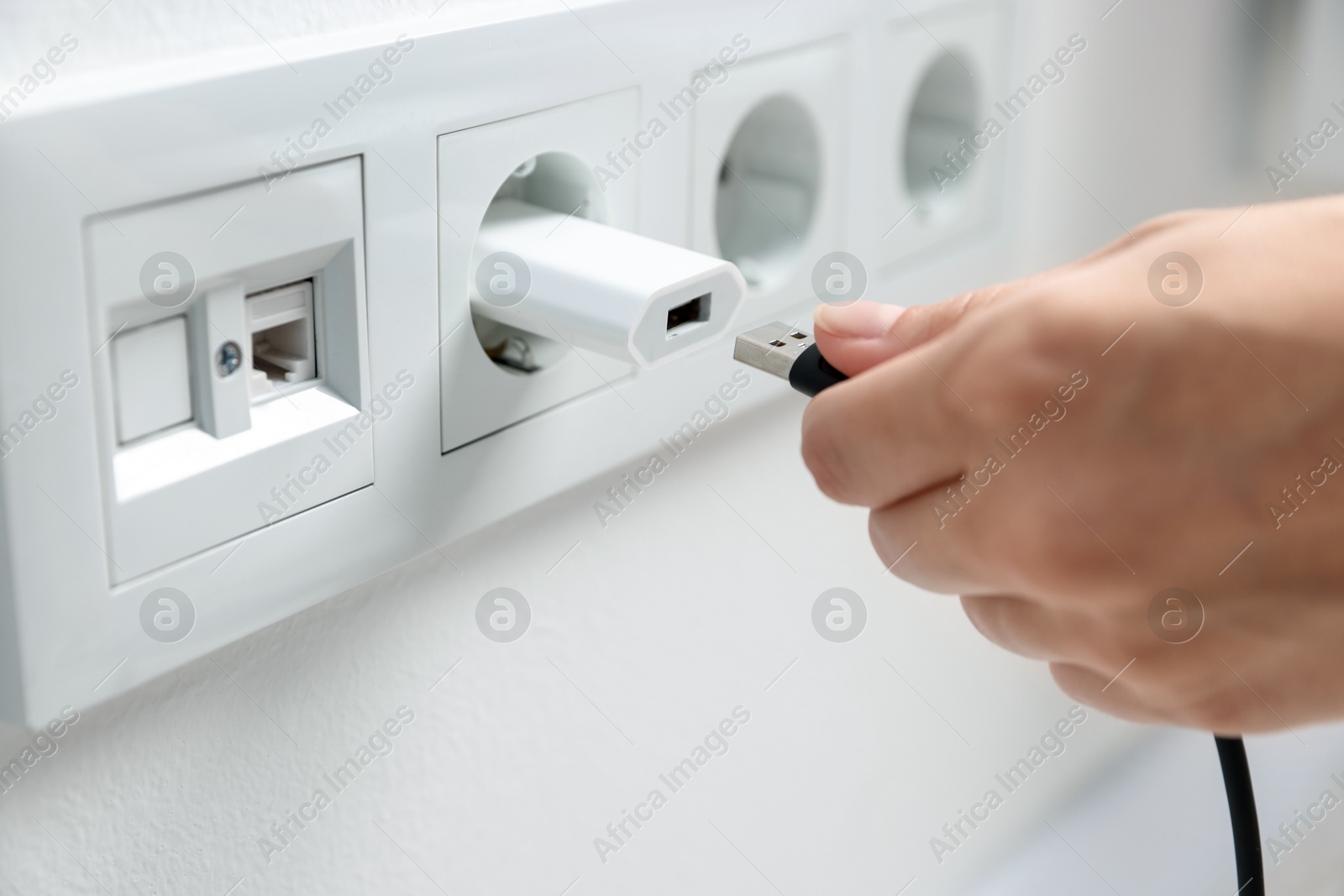 Photo of Woman inserting charge cable into USB adapter indoors, closeup