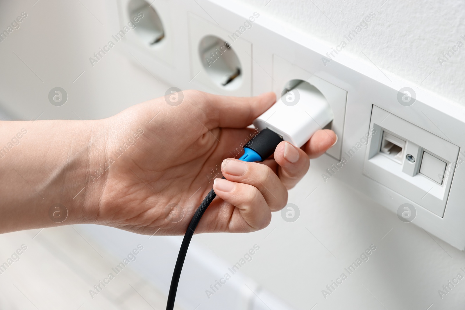 Photo of Woman plugging USB adapter with cable into electric socket on white wall, closeup