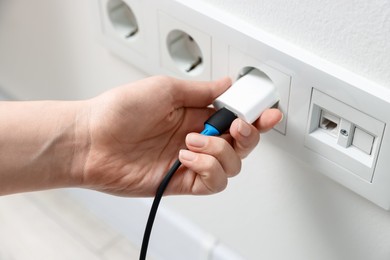 Photo of Woman plugging USB adapter with cable into electric socket on white wall, closeup