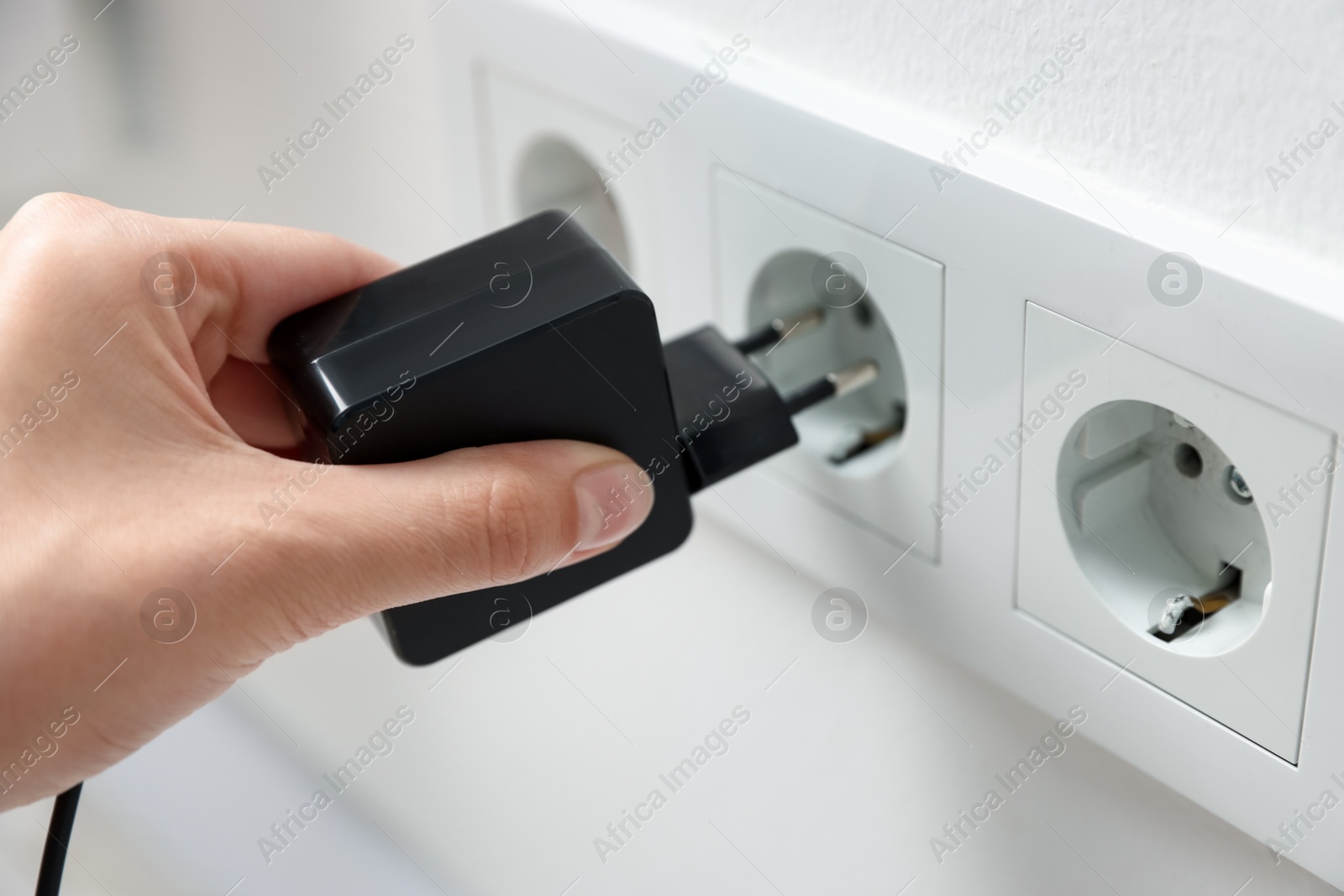Photo of Woman plugging USB adapter with cable into electric socket on white wall, closeup