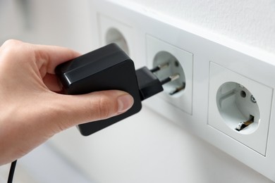 Photo of Woman plugging USB adapter with cable into electric socket on white wall, closeup