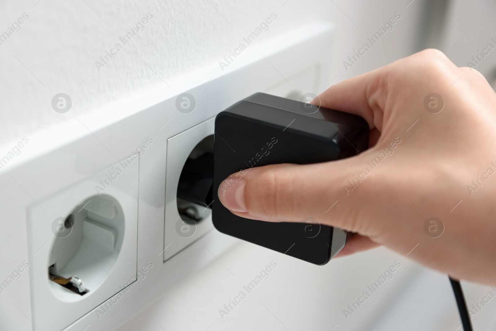 Photo of Woman plugging USB adapter with cable into electric socket on white wall, closeup