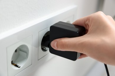 Photo of Woman plugging USB adapter with cable into electric socket on white wall, closeup