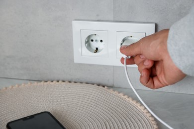 Photo of Man plugging USB adapter with cable into electric socket on light grey wall, closeup