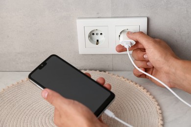Photo of Man plugging smartphone into power socket indoors, closeup