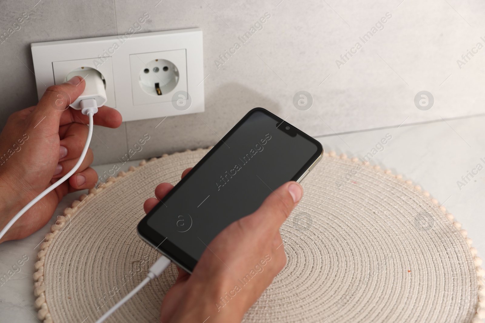 Photo of Man plugging smartphone into power socket indoors, closeup