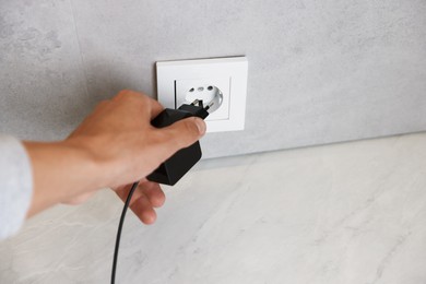 Photo of Man plugging USB adapter with cable into electric socket on grey wall, closeup. Space for text