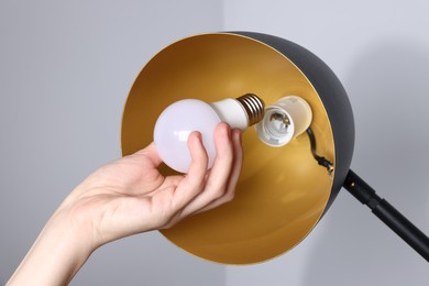 Photo of Woman changing light bulb in lamp near grey wall at home, closeup
