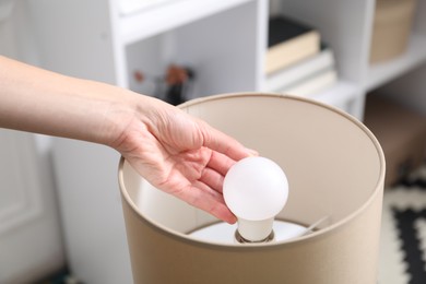 Photo of Woman changing light bulb in lamp at home, closeup