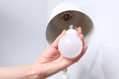 Photo of Woman changing light bulb in lamp near grey wall at home, closeup