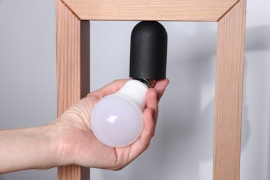 Photo of Woman changing light bulb in lamp near grey wall at home, closeup
