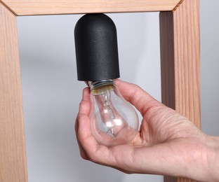 Photo of Woman changing light bulb in lamp near grey wall at home, closeup
