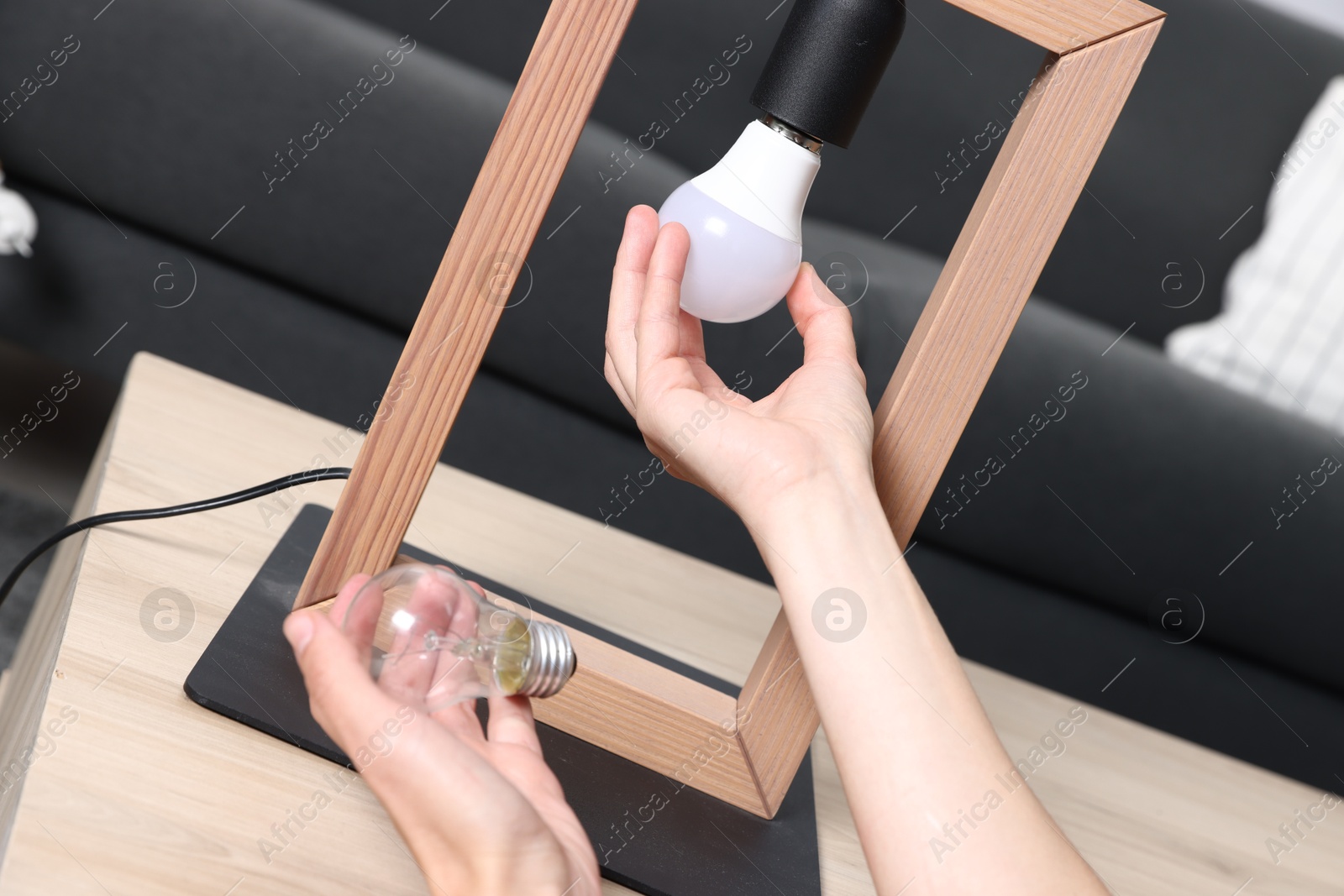Photo of Woman changing light bulb in lamp at wooden table indoors, closeup