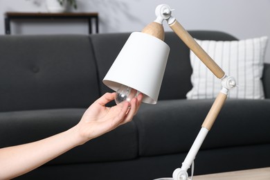 Photo of Woman changing light bulb in lamp at home, closeup