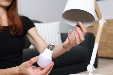 Photo of Woman changing light bulb in lamp at home, closeup