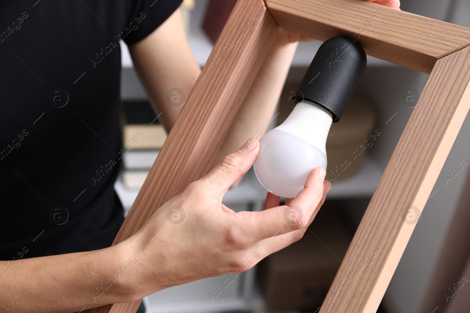 Photo of Woman changing light bulb in lamp at home, closeup