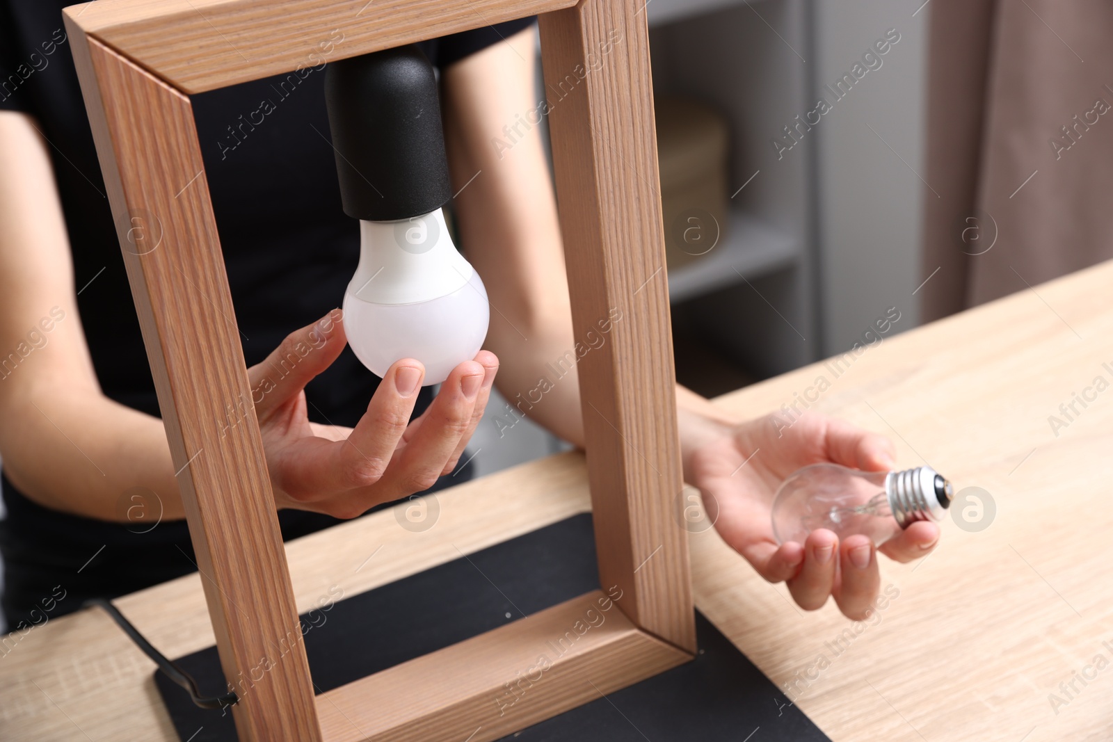 Photo of Woman changing light bulb in lamp at wooden table indoors, closeup