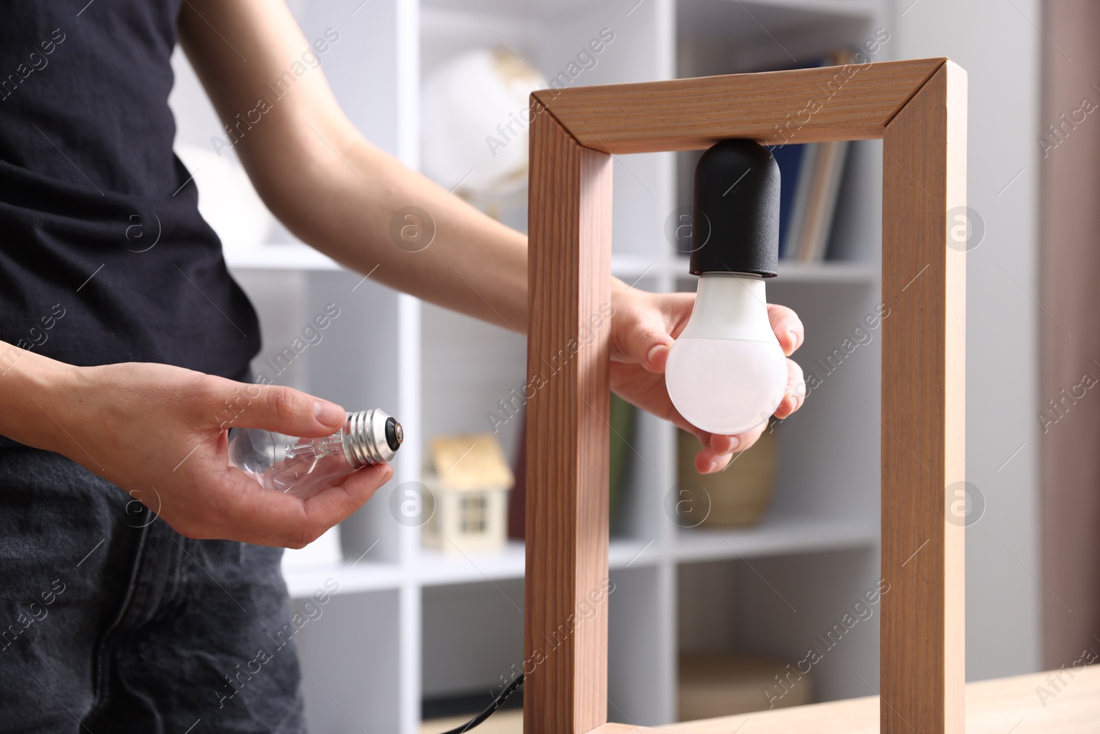 Photo of Woman changing light bulb in lamp at home, closeup