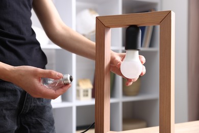 Photo of Woman changing light bulb in lamp at home, closeup