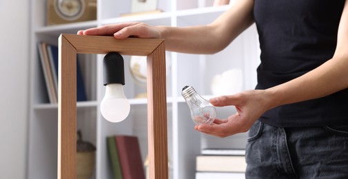 Photo of Woman changing light bulb in lamp at home, closeup