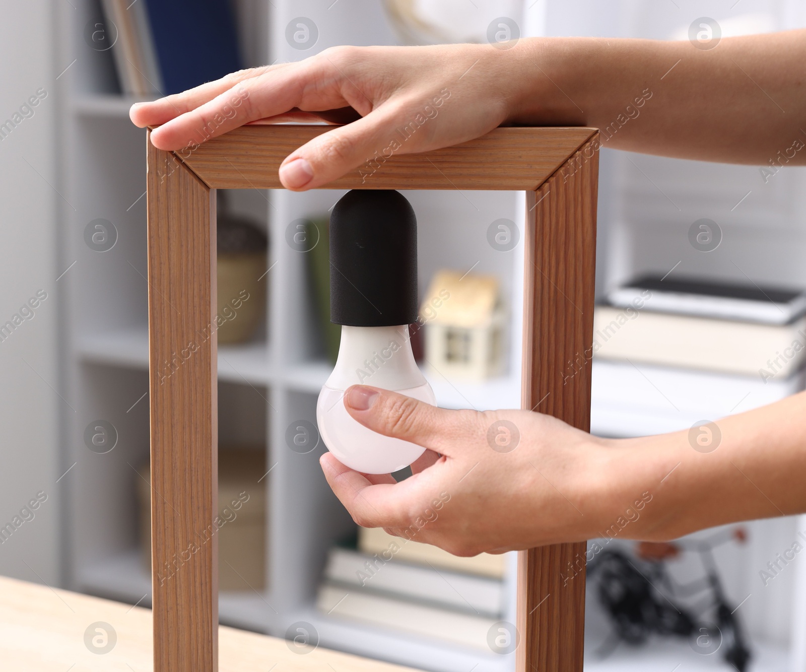Photo of Woman changing light bulb in lamp at table indoors, closeup