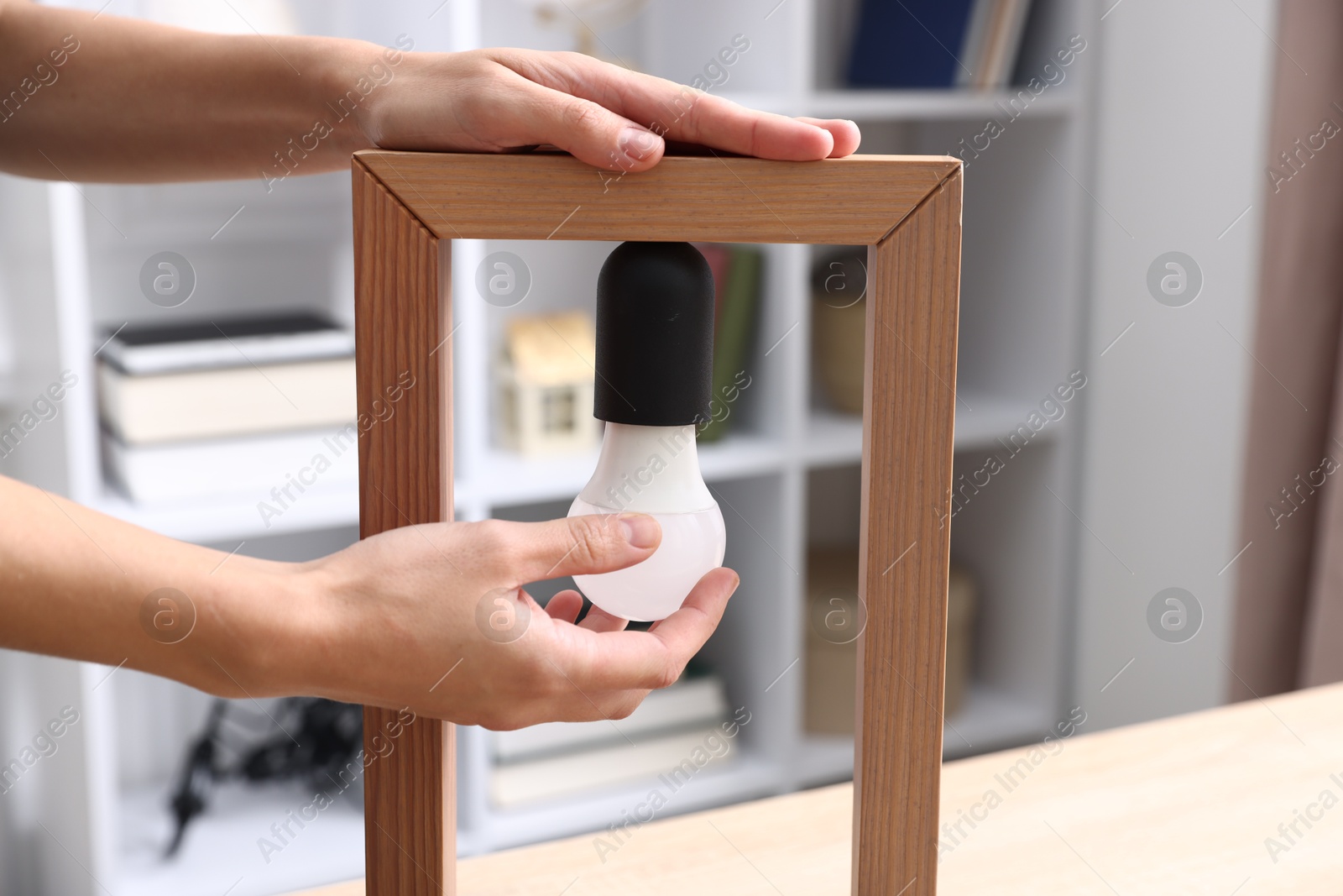 Photo of Woman changing light bulb in lamp at table indoors, closeup