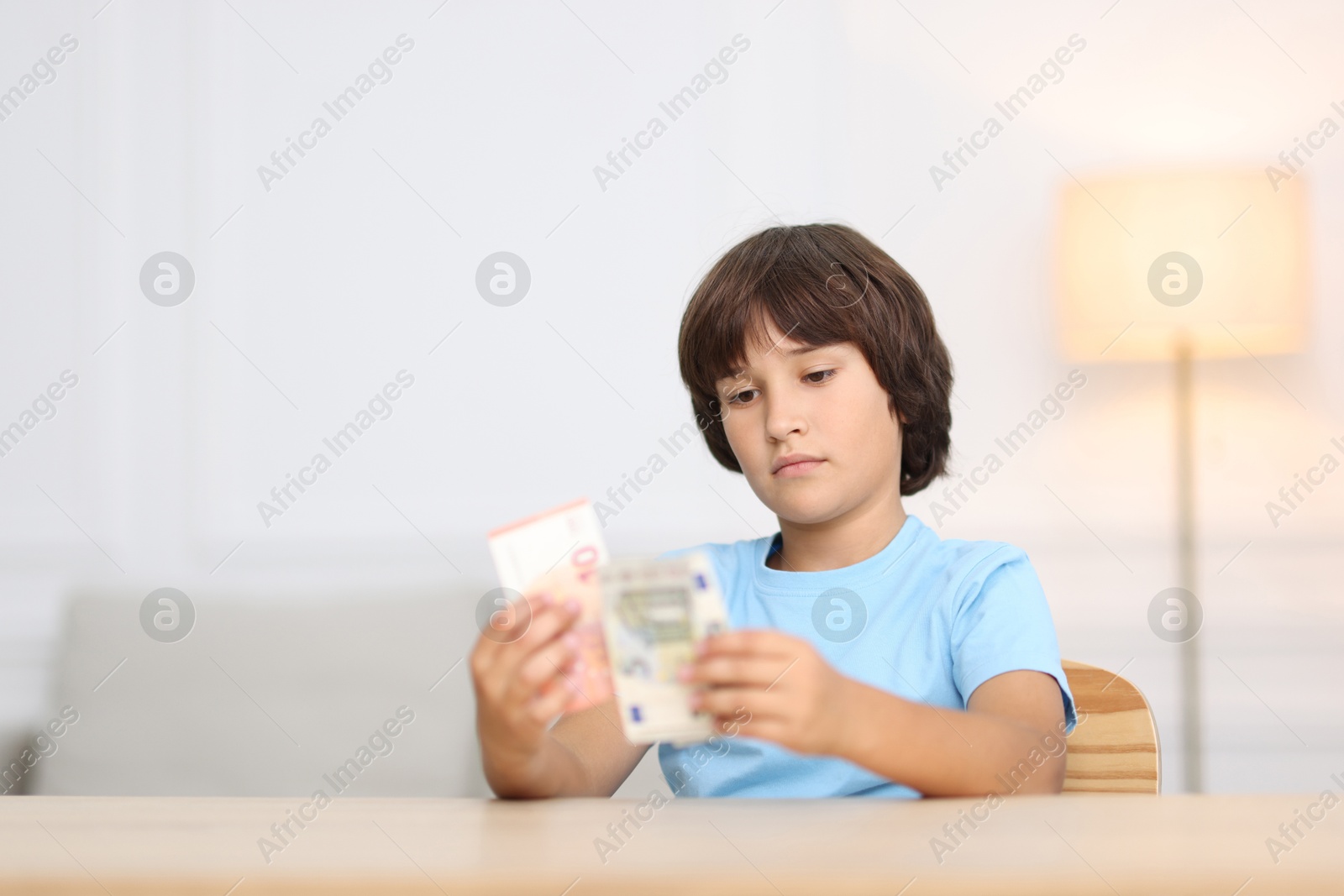 Photo of Boy with pocket money at wooden table indoors. Space for text