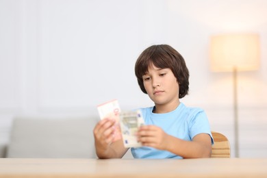 Photo of Boy with pocket money at wooden table indoors. Space for text