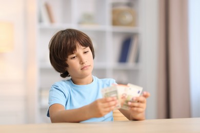 Photo of Boy with pocket money at wooden table indoors. Space for text