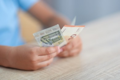 Photo of Boy with pocket money at wooden table indoors, closeup