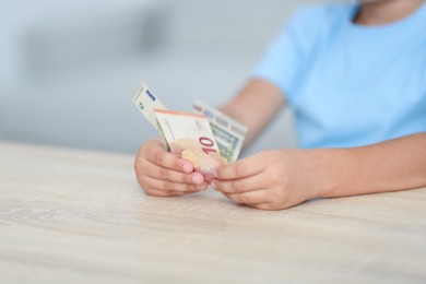 Photo of Boy with pocket money at wooden table indoors, closeup
