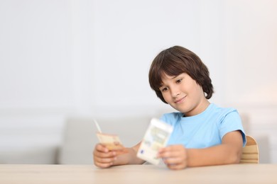 Photo of Boy with pocket money at wooden table indoors. Space for text