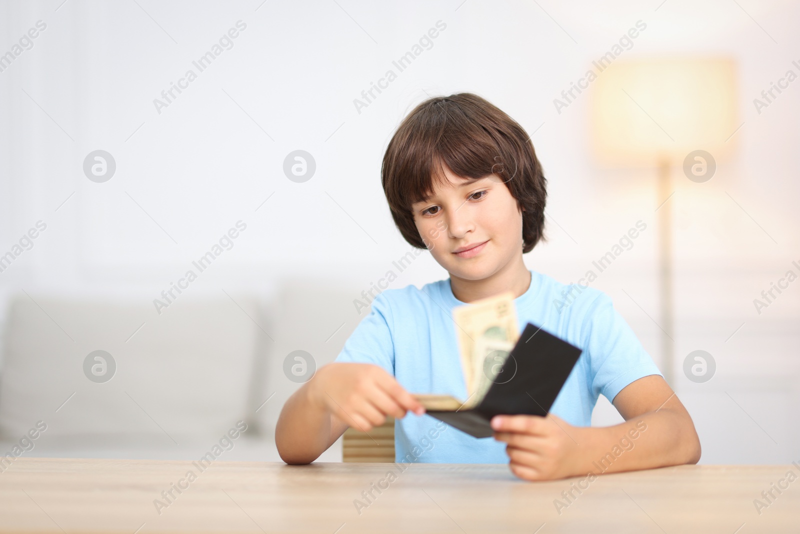 Photo of Boy with pocket money at wooden table indoors. Space for text