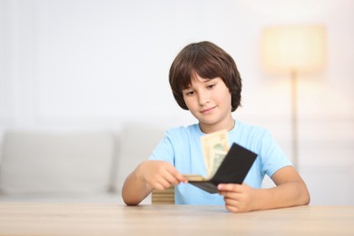Photo of Boy with pocket money at wooden table indoors. Space for text