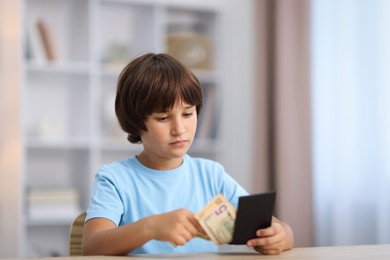 Photo of Boy with pocket money at wooden table indoors. Space for text