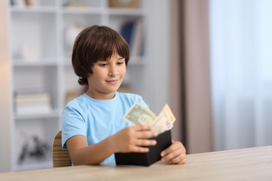 Photo of Boy with pocket money at wooden table indoors. Space for text