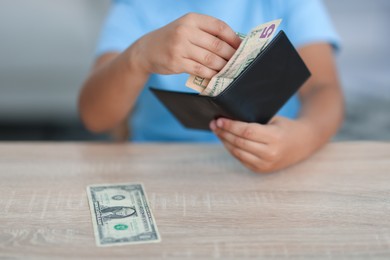 Photo of Boy with pocket money at wooden table indoors, closeup
