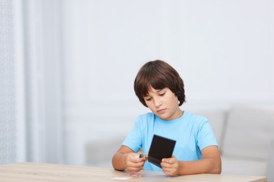 Photo of Boy with pocket money at wooden table indoors. Space for text