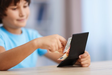 Photo of Boy with pocket money at wooden table indoors, selective focus