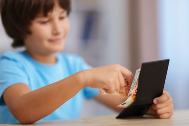 Photo of Boy with pocket money at wooden table indoors, selective focus